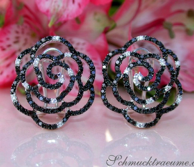 Schwarze Diamant-Rosen Ohrstecker mit weißer Verzierung, vor rosa Blüten. Schwarze Diamant-Rosen Ohrstecker mit weißer Verzierung, vor rosa Blüten.