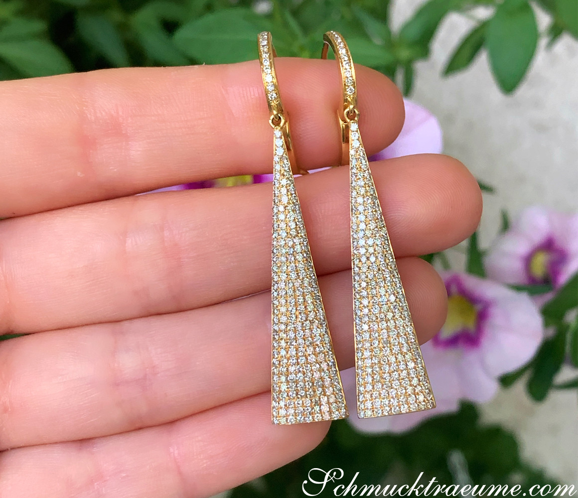 Gelbgold 585 Ohrgehänge mit Diamanten in Hand vor Blüten.