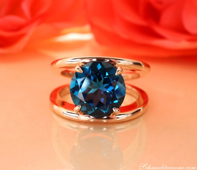 Blautopas-Ring in Roségold 585, minimalistisch gestaltet, auf rotem Hintergrund Blautopas-Ring in Roségold 585, minimalistisch gestaltet, auf rotem Hintergrund