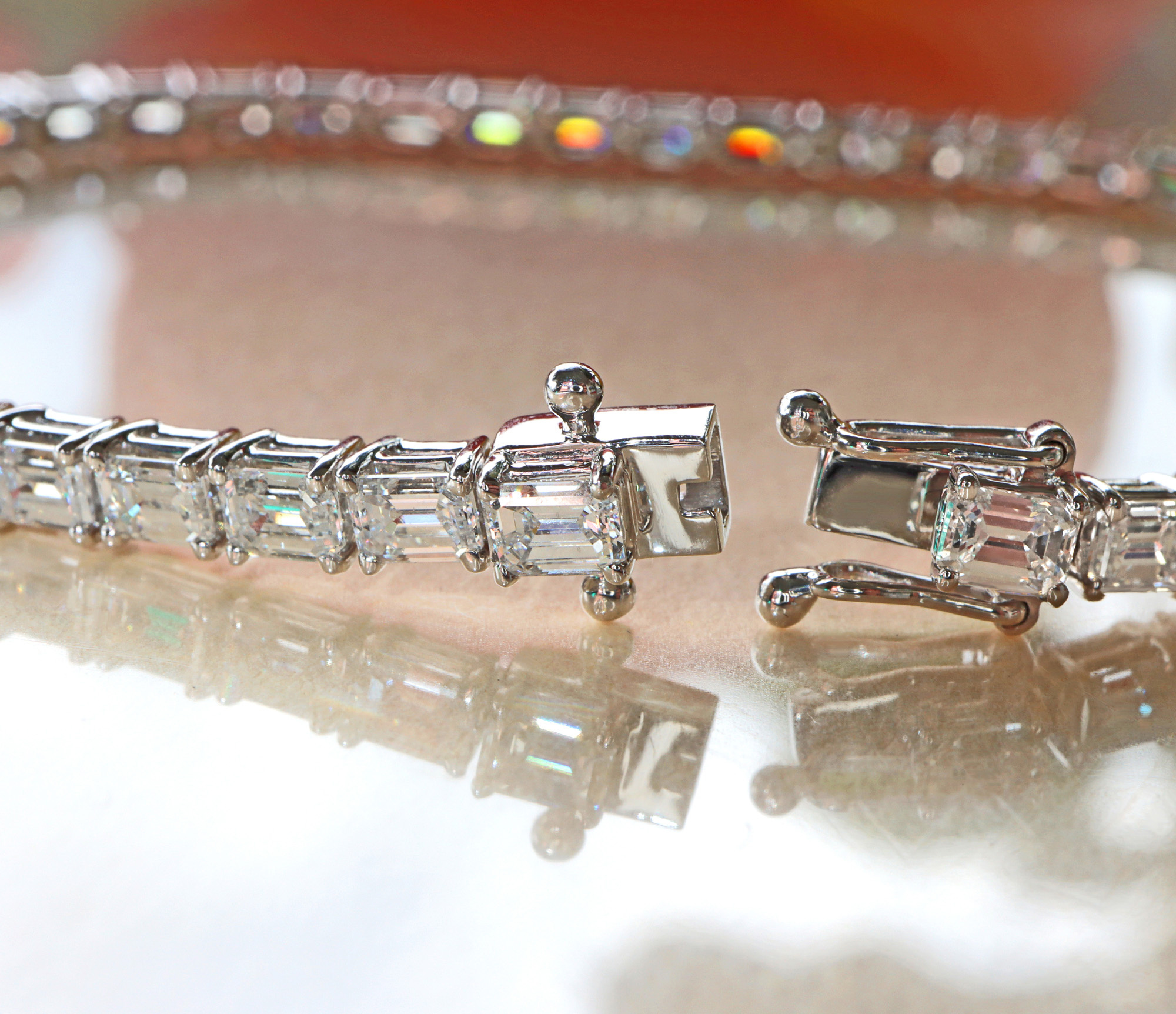 Detailliertes Tennisarmband aus Weißgold mit Smaragdschliff-Diamanten, glänzende Schließe, reflektierender Untergrund.