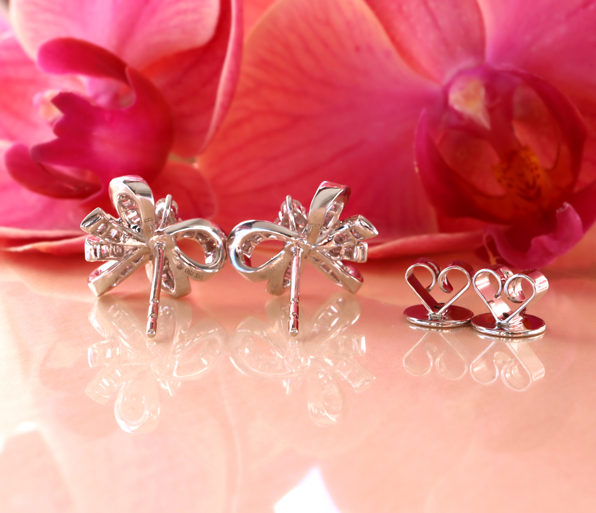 Silberne Schleifen-Ohrstecker mit Brillanten auf rosafarbenem Hintergrund
