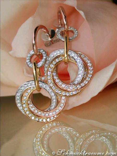 Dreifach verschlungene Goldkreis-Ohrgehänge mit Brillanten, Detailaufnahme, rosa Blüte im Hintergrund