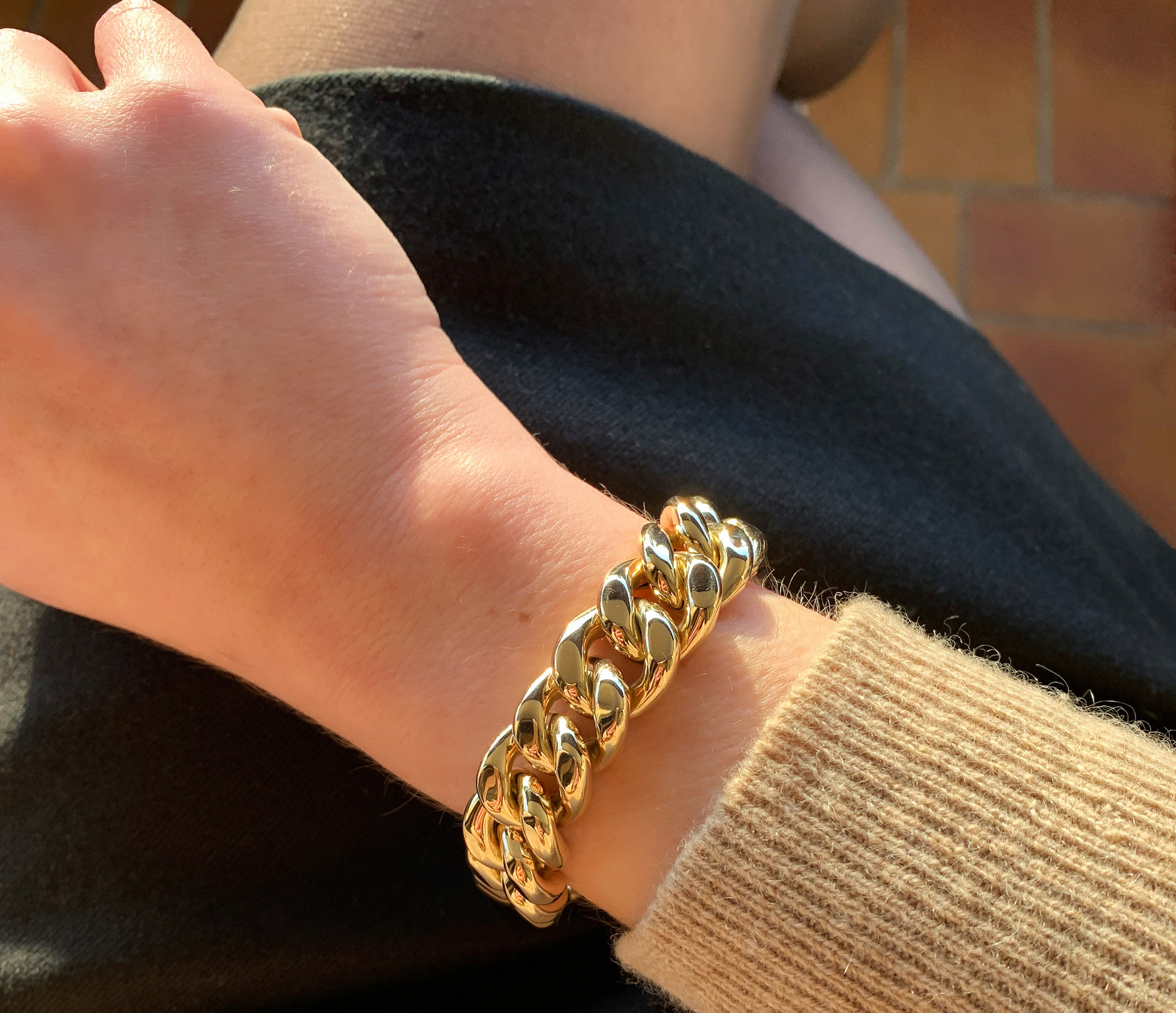 Goldene Panzerarmband auf dem Unterarm, detailreiches Design, sonniger Hintergrund.