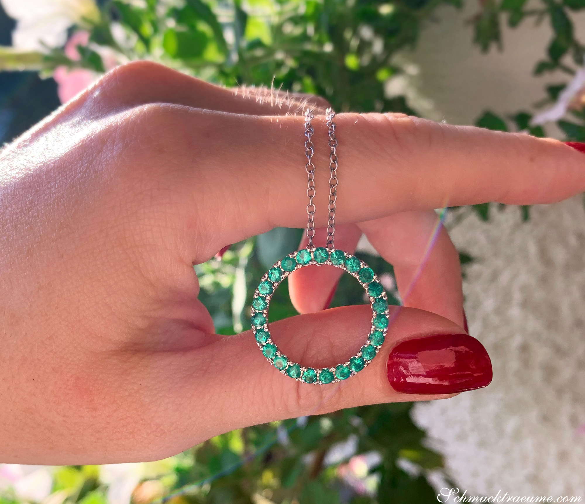 Hand mit rotem Nagellack hält Smaragd-Kreis-Anhänger mit Weißgoldkette