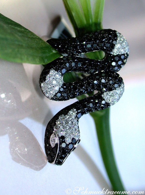 Schwarz-schimmernder Schlangenring mit Diamanten, Detailaufnahme, elegant auf Blatt dargestellt