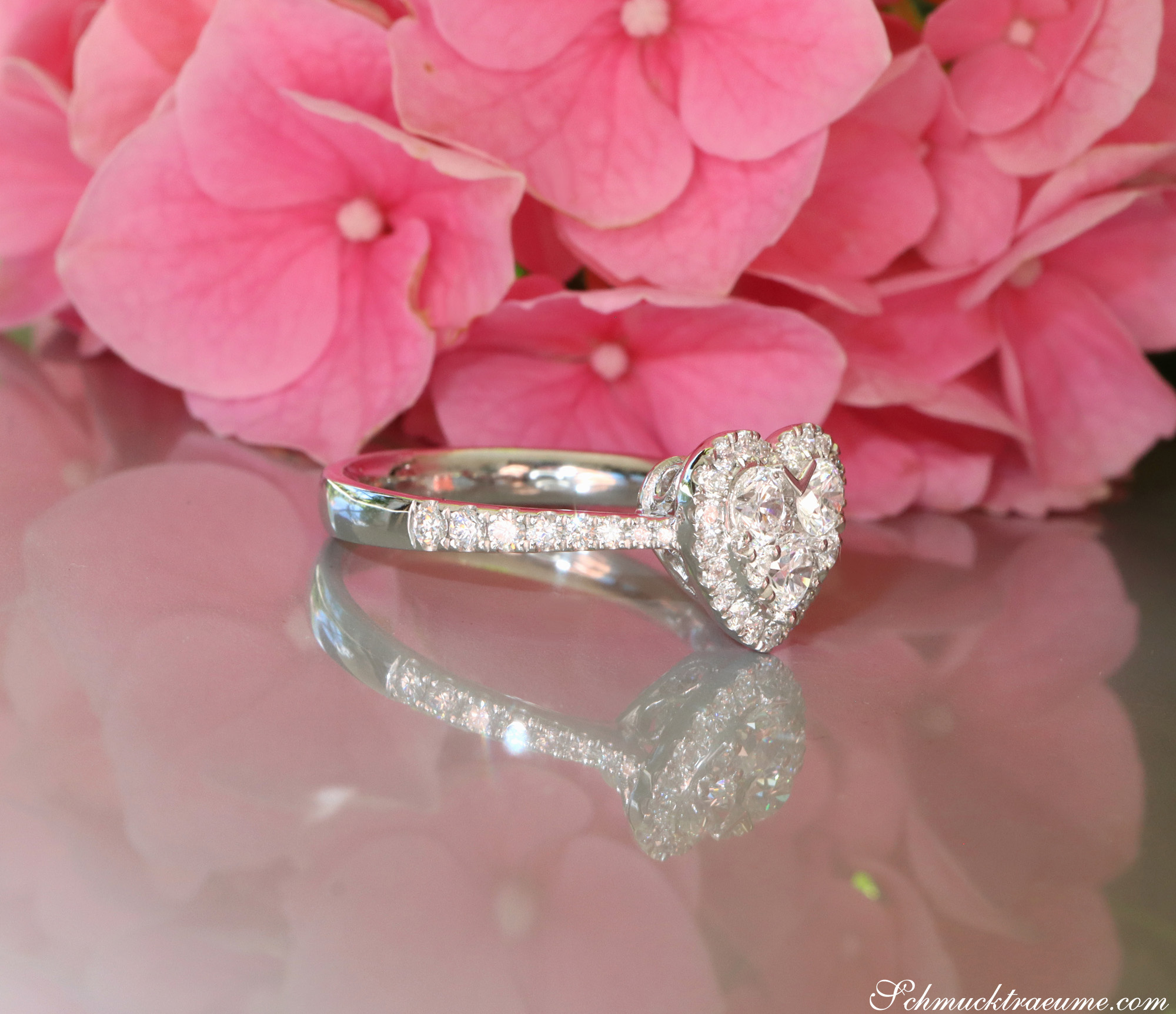 Herzform-Ring mit VS-Brillanten in Weißgold 750, vor rosa Hortensienblüten.