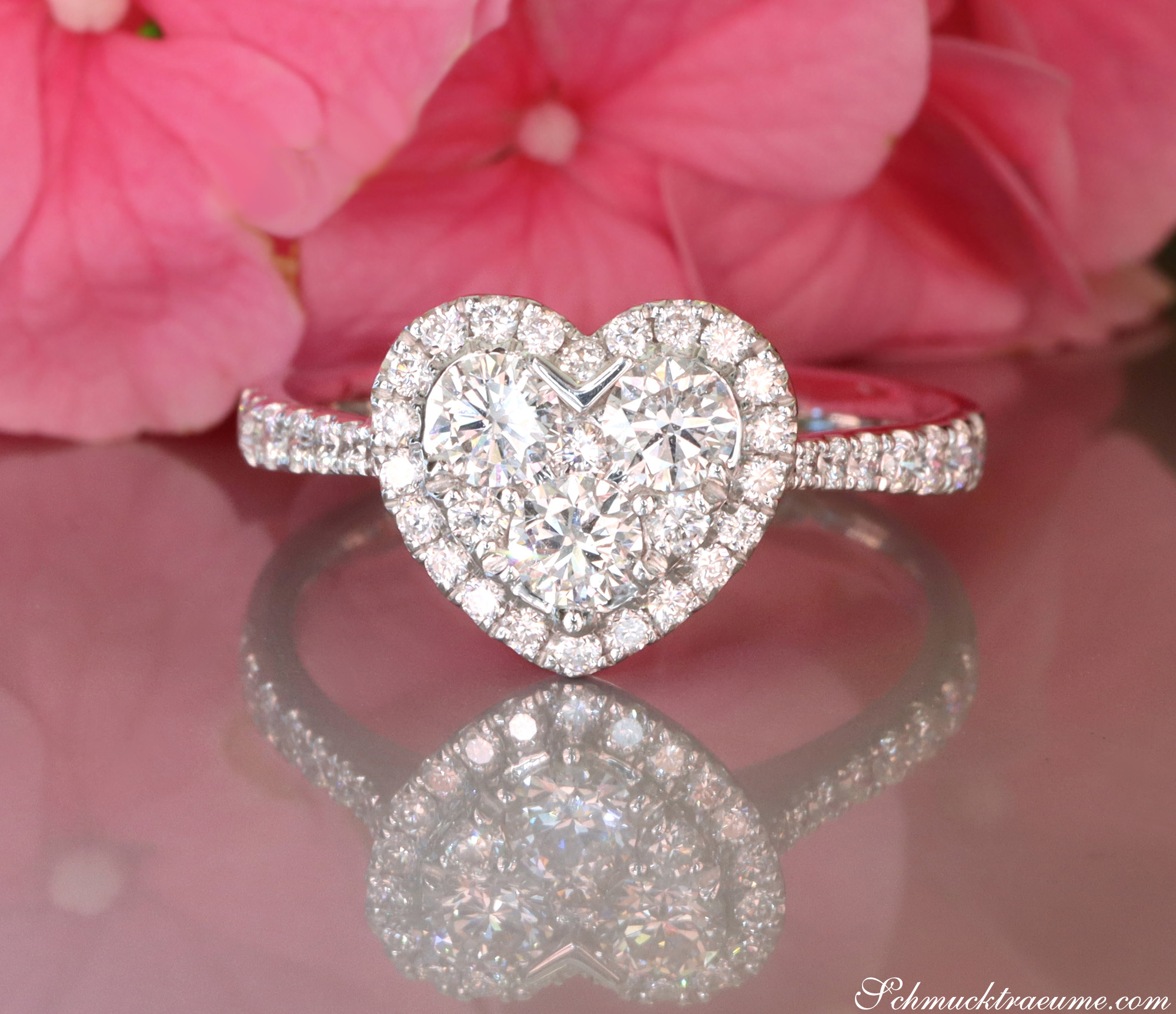Herzformiger Diamantring mit Halo in Weißgold, Detailaufnahme, rosa Blüte im Hintergrund