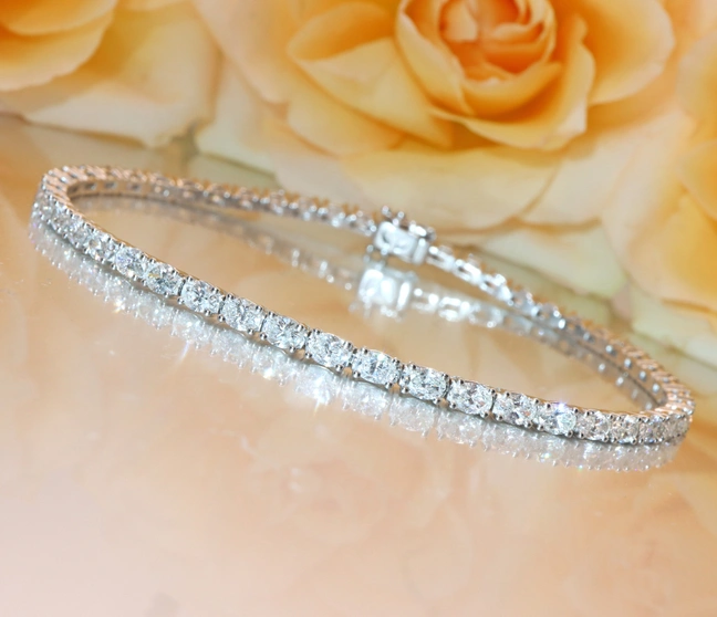 Diamant-Tennisarmband im Ovalschliff auf Rosenblütenhintergrund Diamant-Tennisarmband im Ovalschliff auf Rosenblütenhintergrund