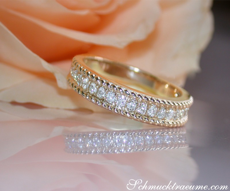 Goldener Diamanterring mit Kordel-Design, Detailaufnahme, Rosenblüte im Hintergrund