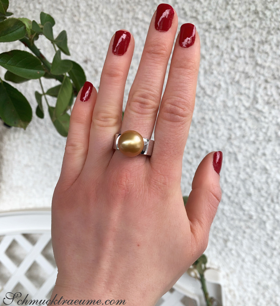 Weißgold-Ring mit goldenen Perle, Nagellack rot, Detailaufnahme Hand vor Pflanze.