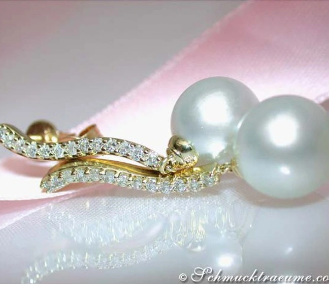 Gelbgold-Ohrringe mit Südseeperlen und Brillanten auf rosa Stoff. Gelbgold-Ohrringe mit Südseeperlen und Brillanten auf rosa Stoff.