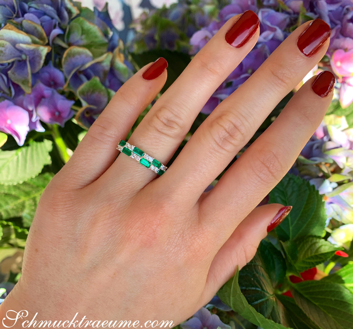 Hand mit roten Nagellack und Smaragd-Brillant-Ring vor Blumen