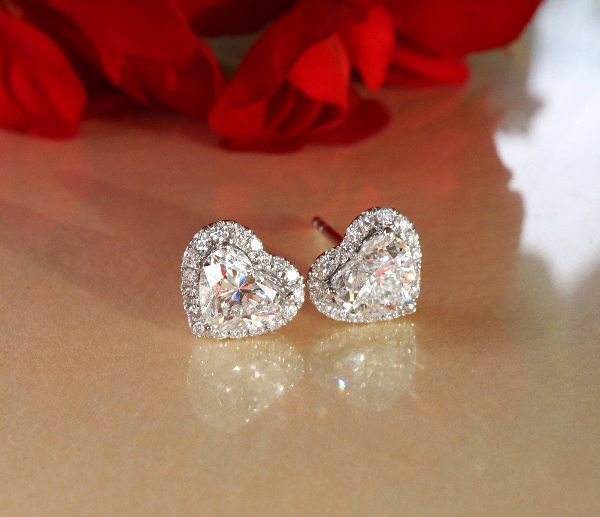 Herzformige Ohrstecker aus Weißgold mit Diamanten, im Hintergrund Rosenblätter.