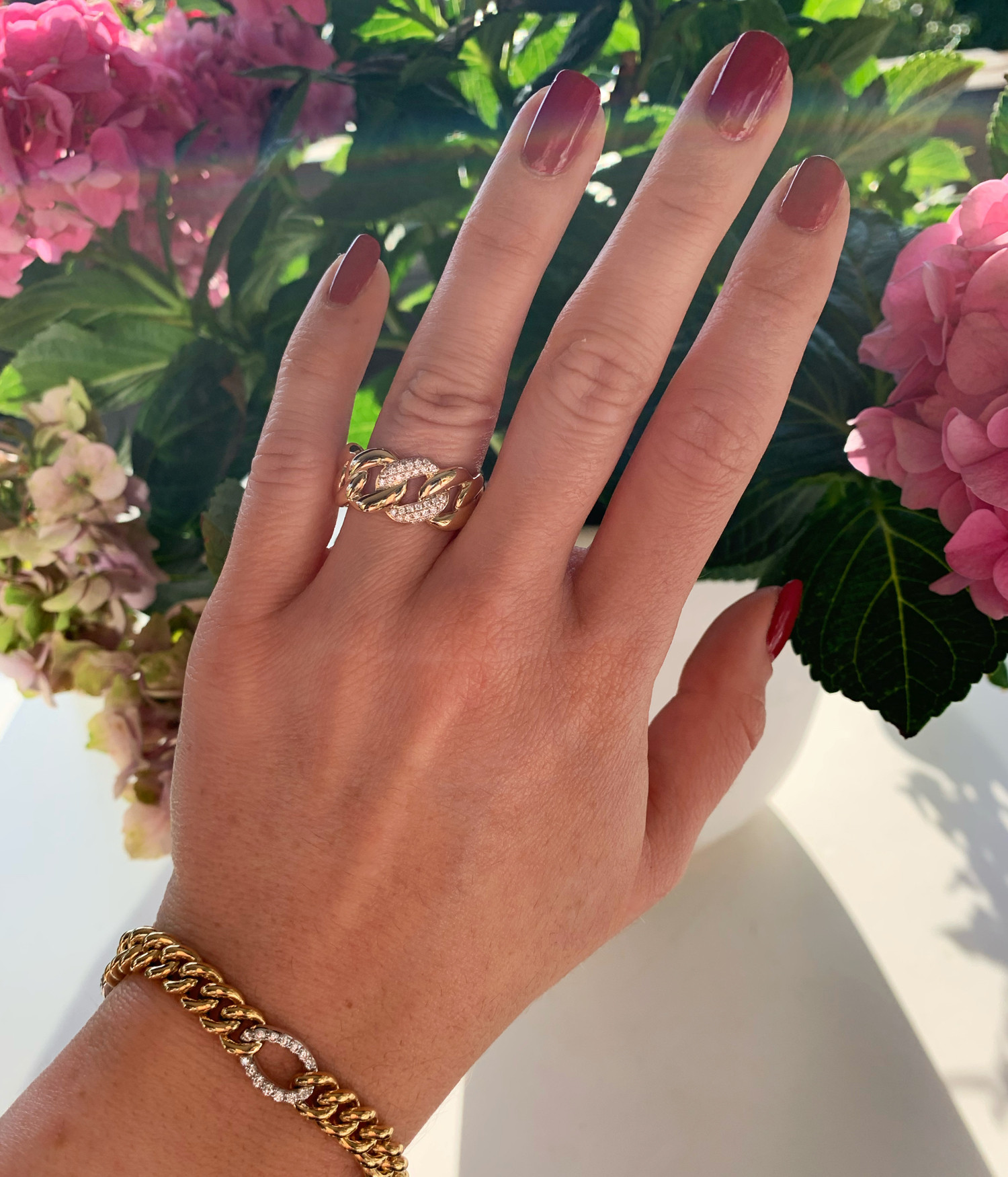 Hand mit Panzerkettengoldring, Nagellack rot, Blumen im Hintergrund