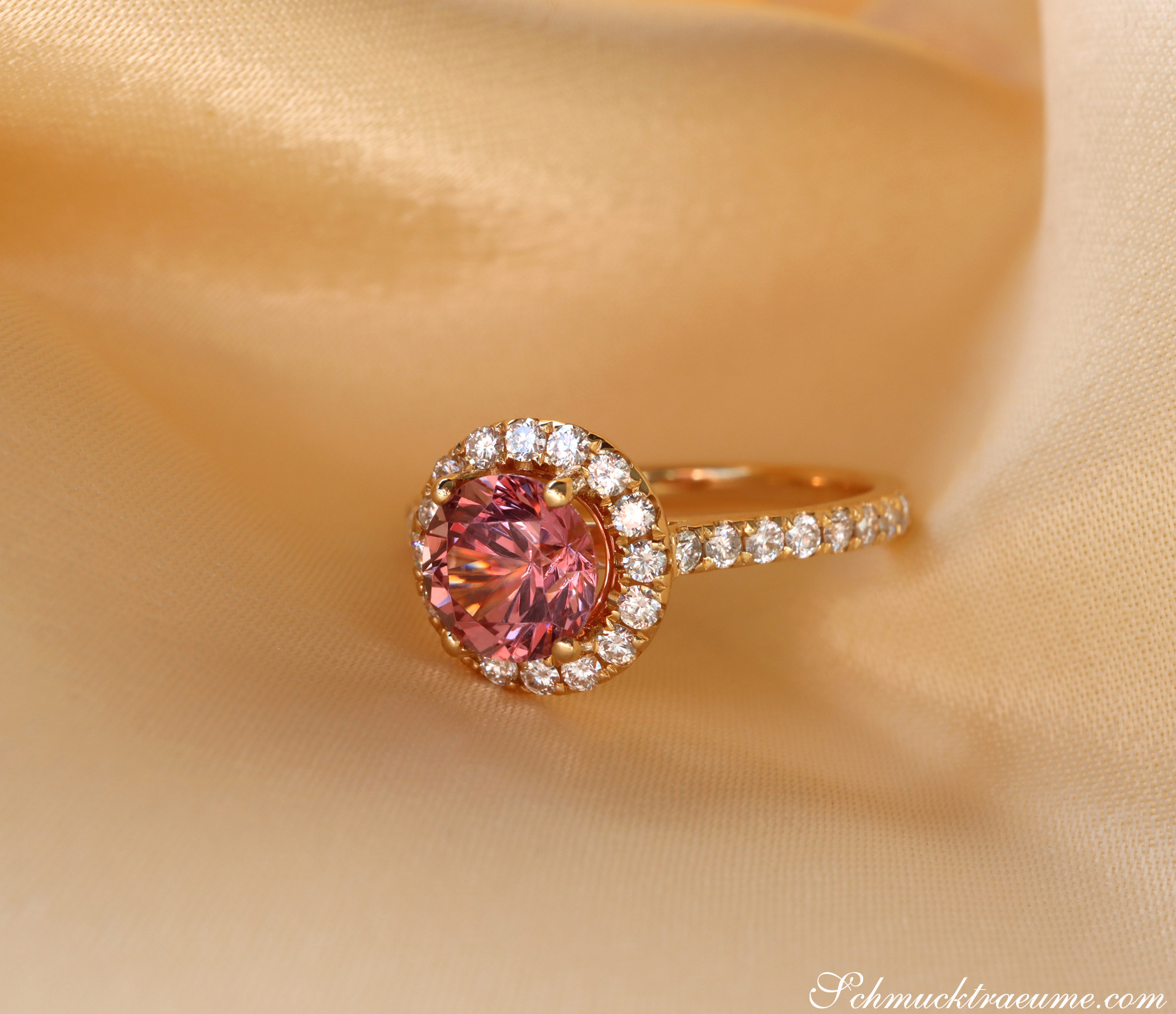 Rosa Granat-Ring mit Diamanten in Gelbgold, detailreich, elegant, auf cremefarbenem Stoff liegend.