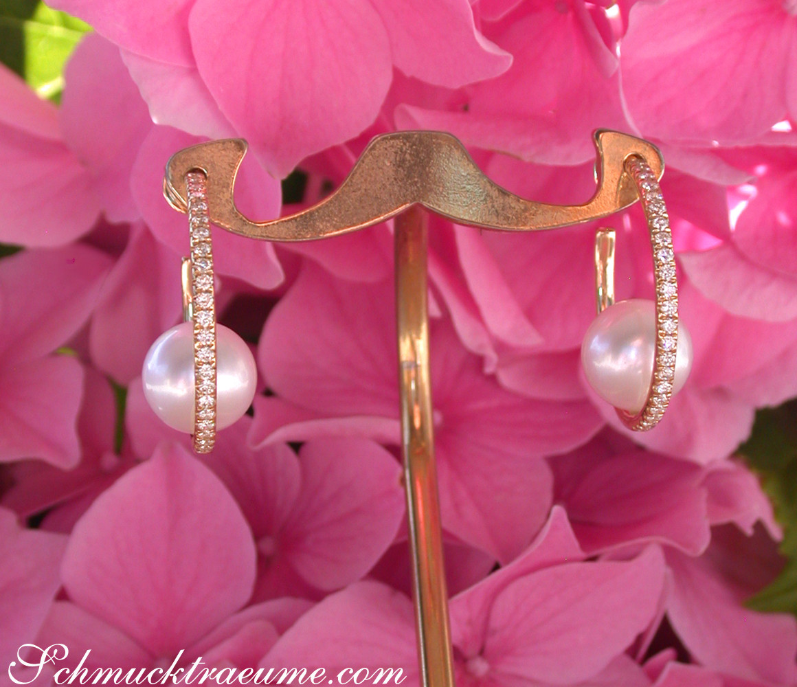 Goldene Creolen mit Perlen und Diamanten vor rosa Blüten.