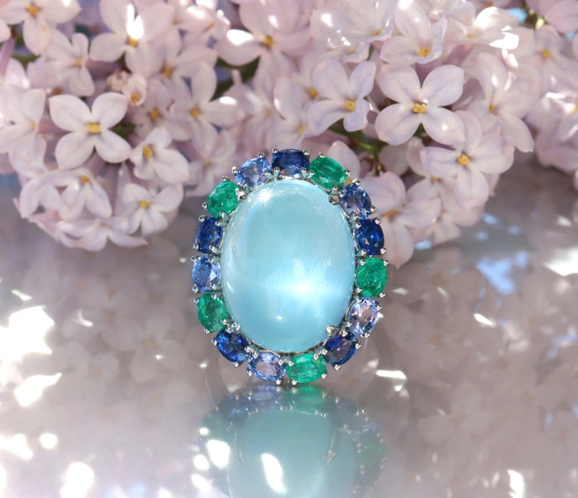 Milky Aquamarin-Ring mit Saphiren und Smaragden auf Lilienblüten-Hintergrund Milky Aquamarin-Ring mit Saphiren und Smaragden auf Lilienblüten-Hintergrund