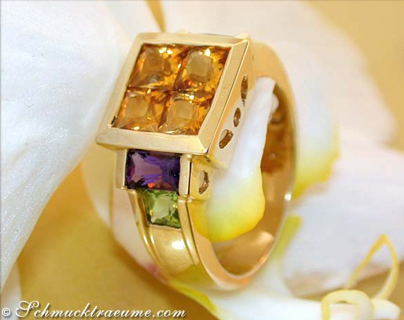 Goldener Citrin-Amethyst-Peridot-Ring, Detailaufnahme, hochwertige Verarbeitung, Orchideenblüte im Hintergrund.