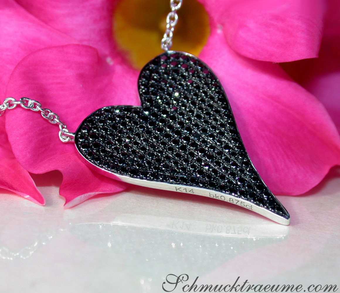 Schwarzer Diamantenherzanhänger mit Kette, Detailaufnahme, rosa Blüten im Hintergrund.