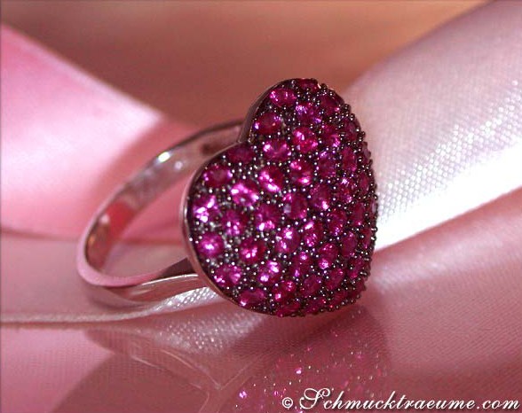 Herzring aus Weißgold 585 mit 1.900 Rubinen, detailreich, auf rosa Seide.