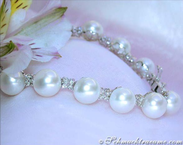 Perlenarmband mit Diamanten auf weicher Stoffoberfläche, Blume im Hintergrund.