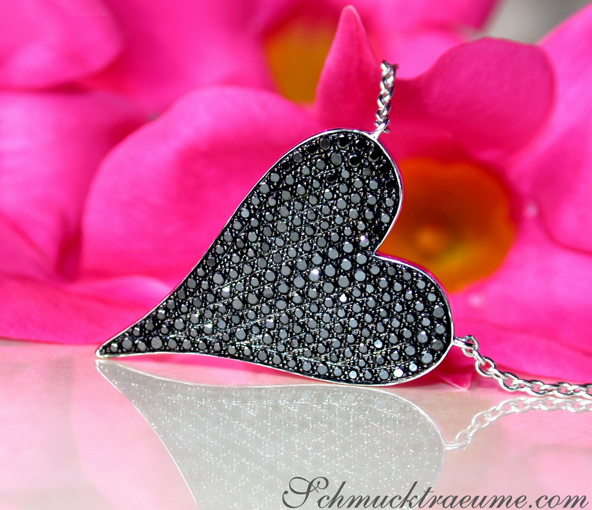 Schwarzer Diamantenherzanhänger auf silberner Kette, vor rosa Blütenblättern.
