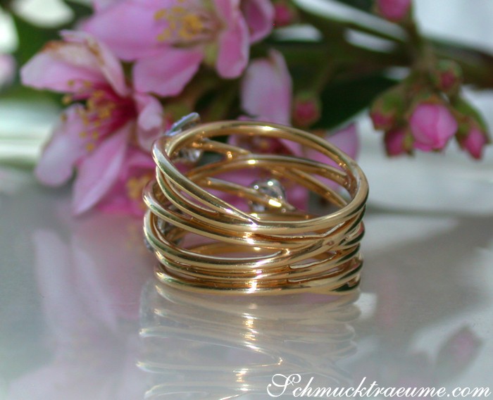 Zarte Mehrreihen-Diamantringe auf glänzender Oberfläche mit rosa Blüten im Hintergrund