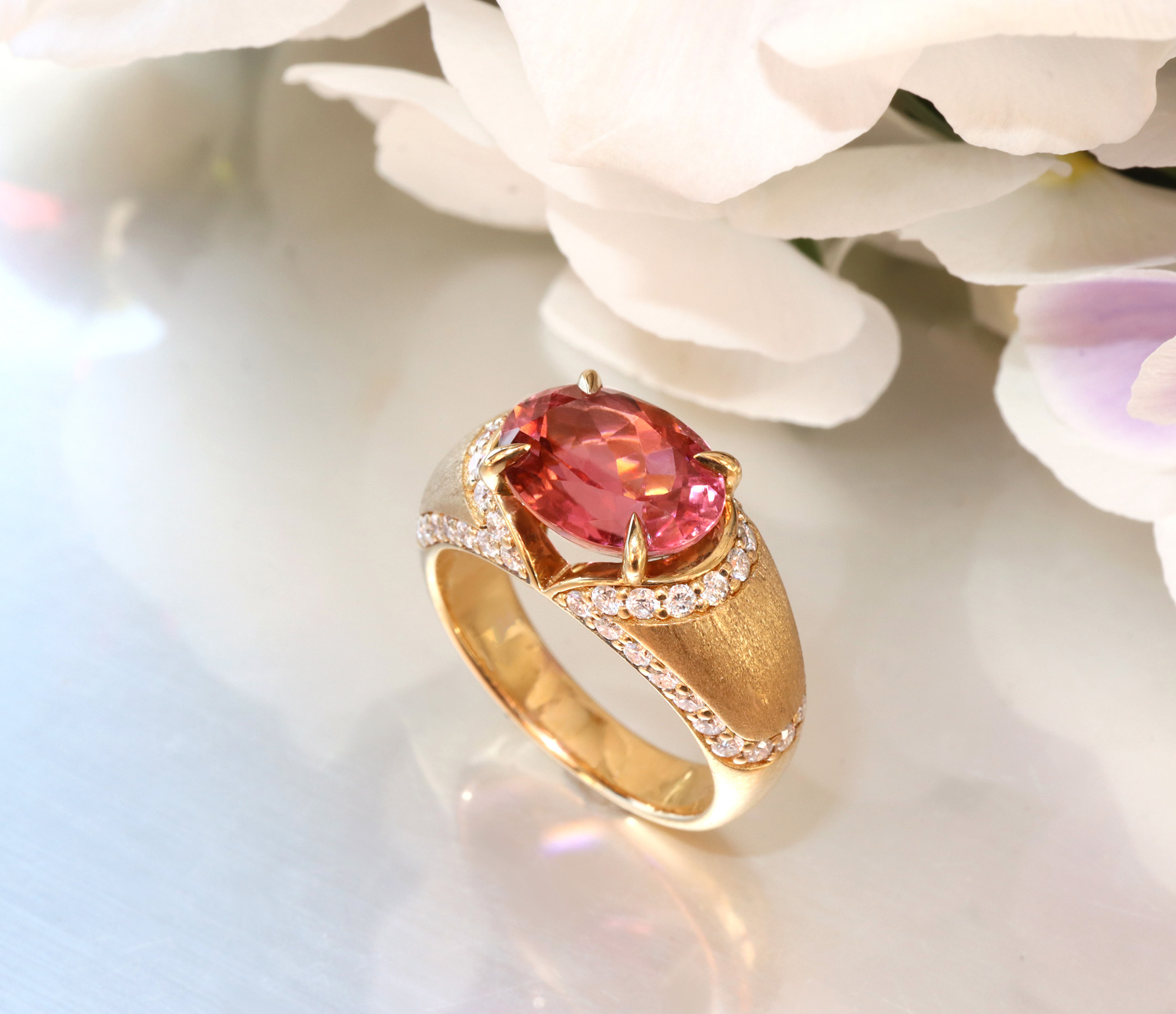 Goldener Ring mit rosa Turmalin und Diamanten, Blumen im Hintergrund