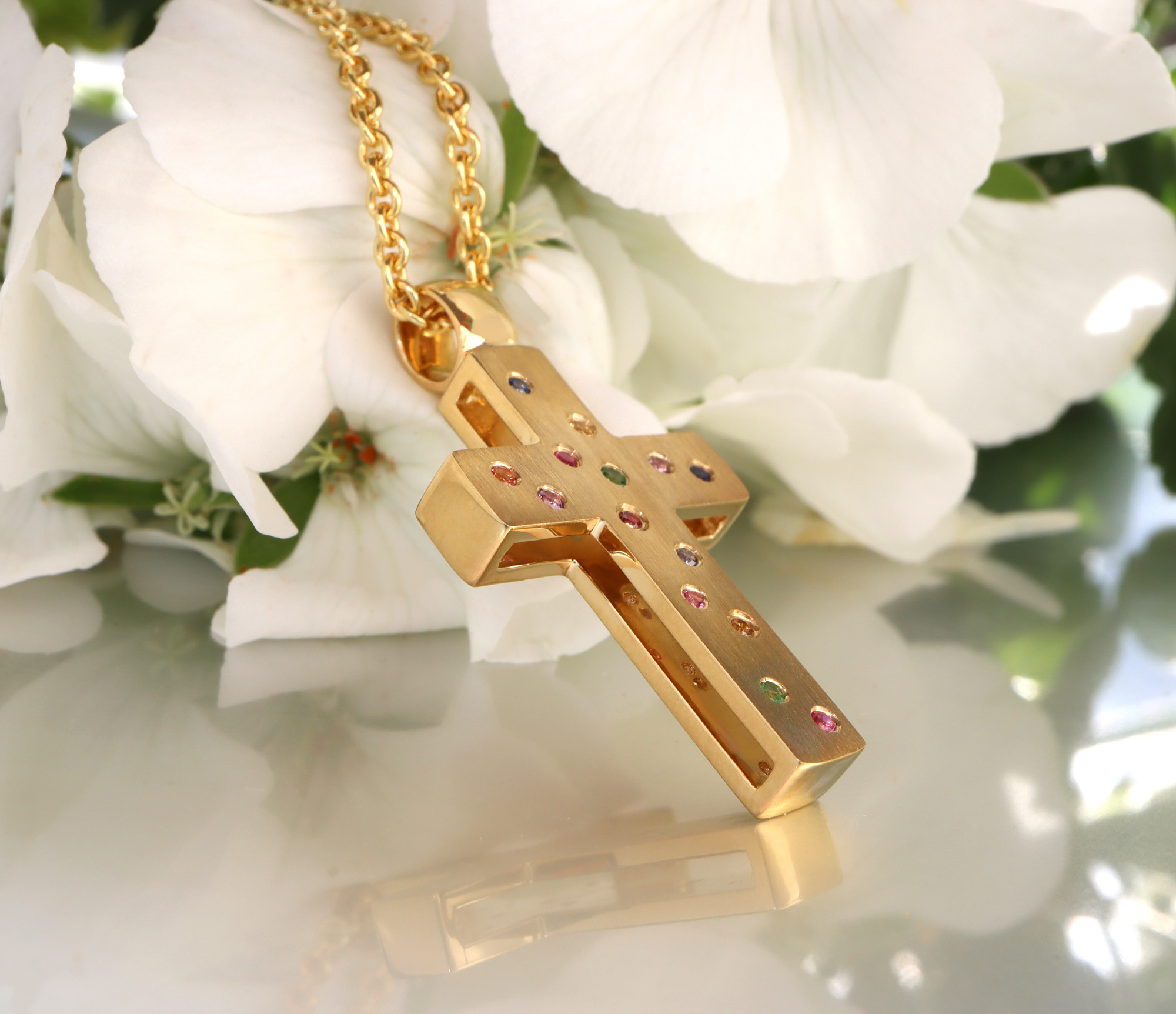 Goldener Kreuzanhänger mit Brillanten und Multicolor Saphiren, Detailaufnahme auf weißem Hintergrund.