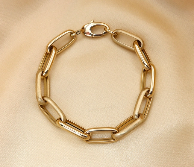 Goldenes Paperclip-Armband aus 585er Gelbgold, glänzend & satiniert, liegt auf seidigem Stoff. Goldenes Paperclip-Armband aus 585er Gelbgold, glänzend & satiniert, liegt auf seidigem Stoff.