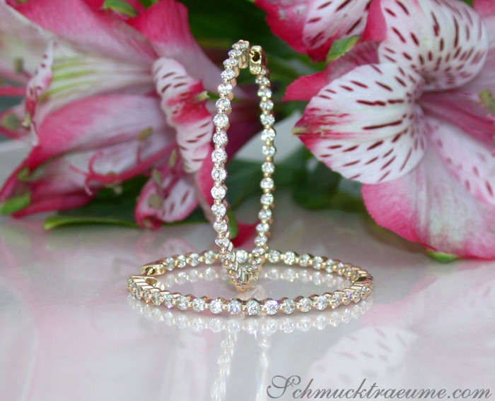 Goldene Creolen mit Diamanten auf Blumenhintergrund