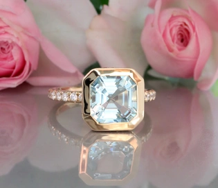 Aquamarin-Ring in 585er Gelbgold, detailreich, umgeben von Rosenblüten.