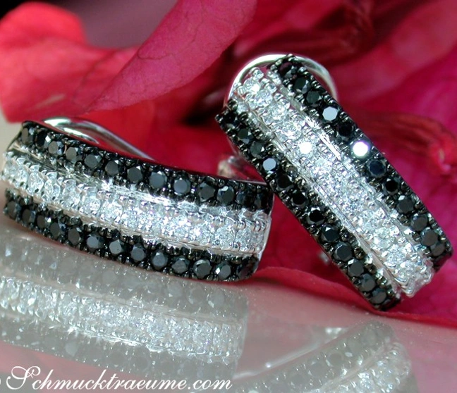 Schwarz-weiße Diamantohrringe in Weißgold, elegant auf Rosenblatt-Hintergrund Schwarz-weiße Diamantohrringe in Weißgold, elegant auf Rosenblatt-Hintergrund