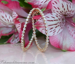 Goldene Creolen mit Diamanten auf Blütenhintergrund