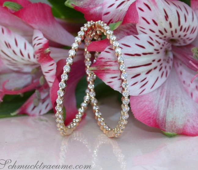 Goldene Creolen mit Diamanten auf Blütenhintergrund Goldene Creolen mit Diamanten auf Blütenhintergrund