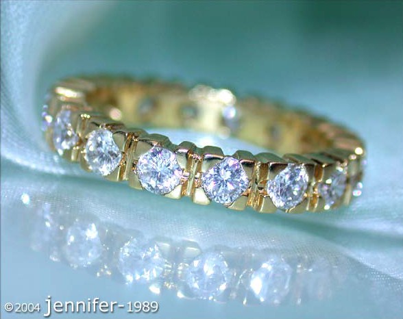 Goldener Diamant Memory Ring mit funkelnden Steinen auf weichem Stoff, Detailaufnahme.