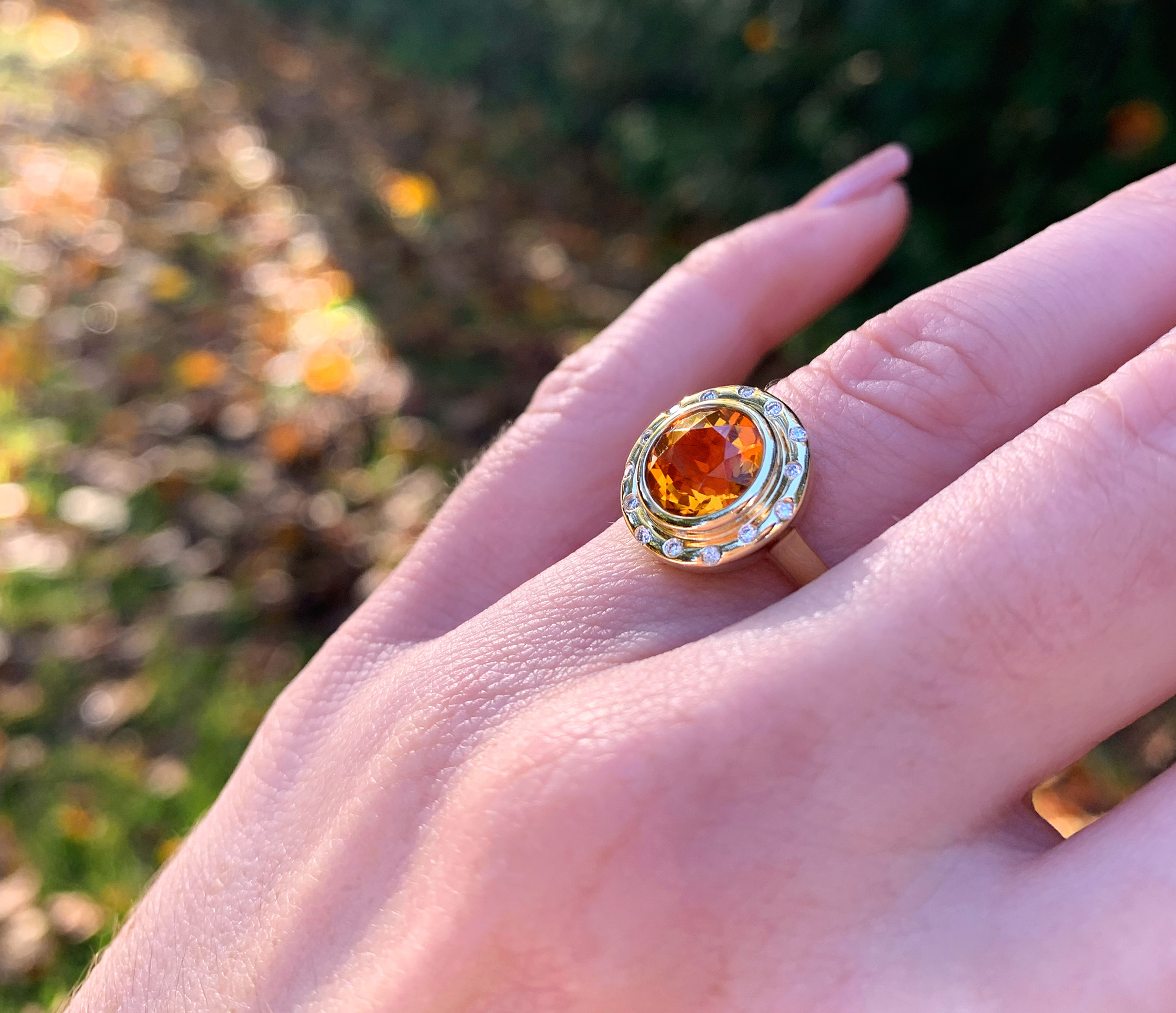 Goldener Citrin-Ring mit umlaufenden Brillanten auf Hand vor Naturhintergrund