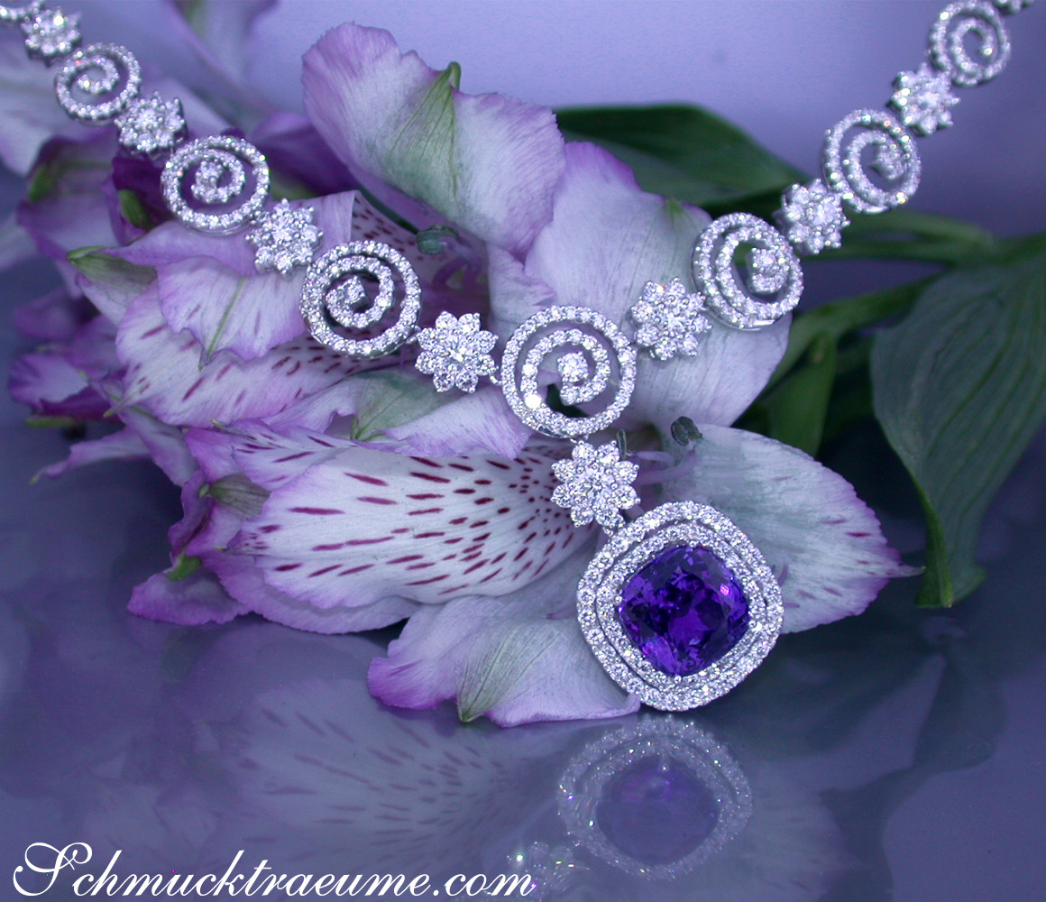 Silbernes Tansanit-Collier mit Brillanten, spiralförmige Verzierungen, lila Blüten im Hintergrund.