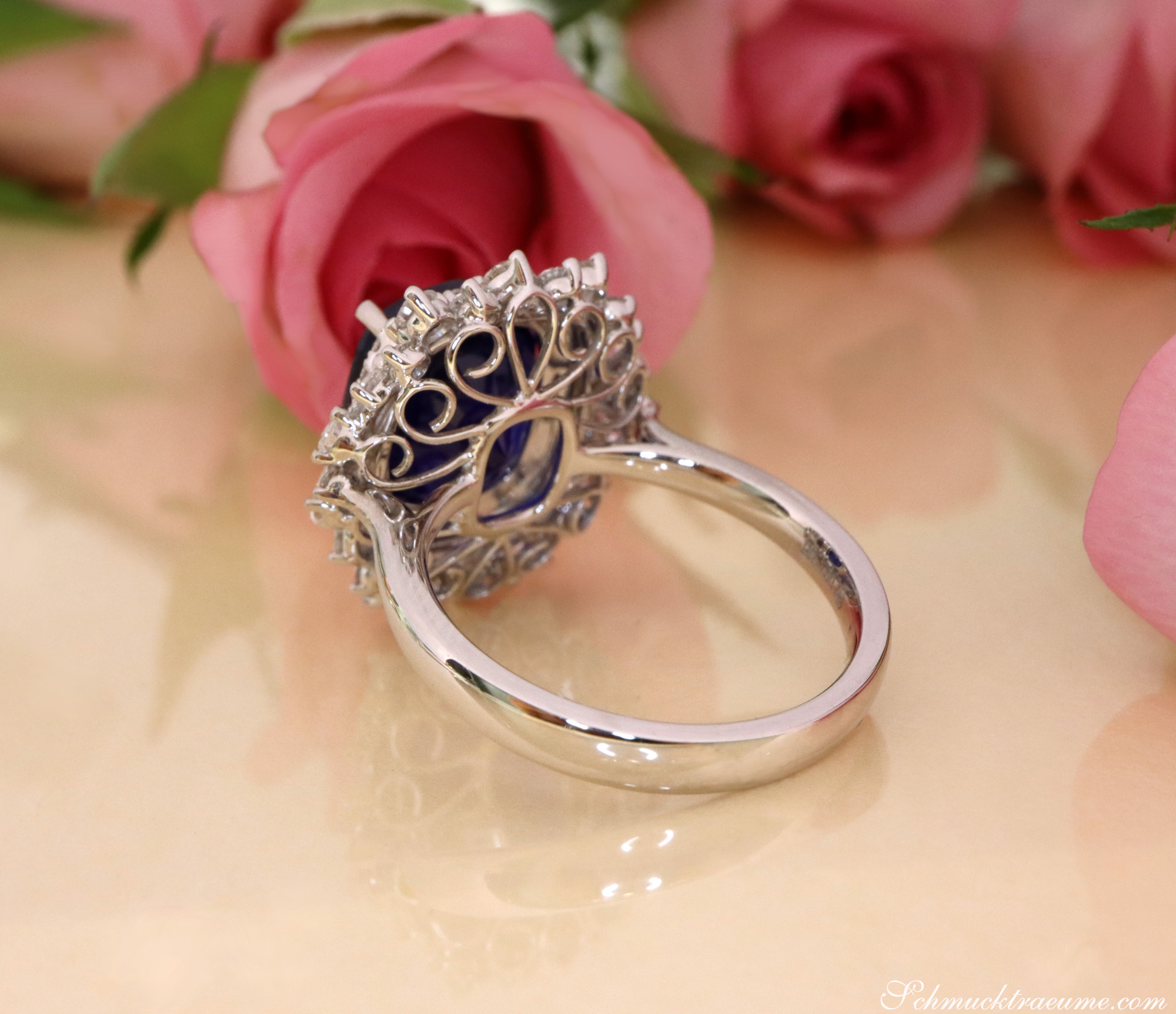 Schmuckring mit Ceylon Saphir und Diamanten, filigrane Verzierung, Rosen im Hintergrund