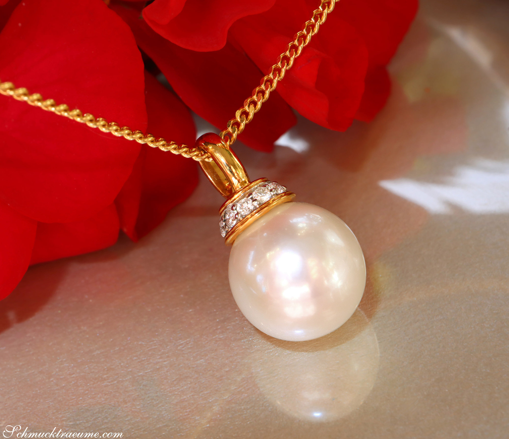 Goldkette mit Perlenanhänger und Brillanten vor roten Rosenblättern