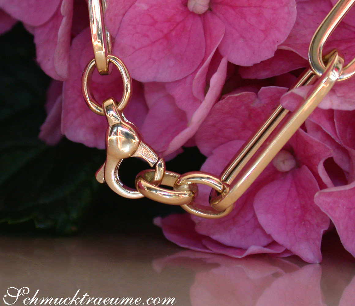 Goldene Paperclip-Armband-Detail mit rosafarbenen Hortensienblüten im Hintergrund