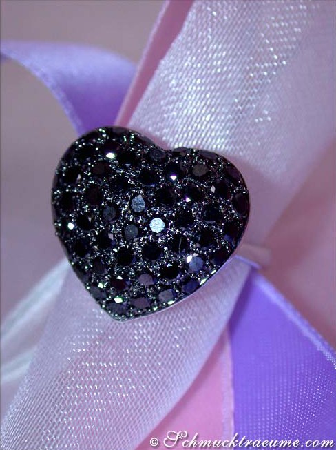 Herzformiger Ring mit schwarzen Diamanten auf schimmerndem Satinband.