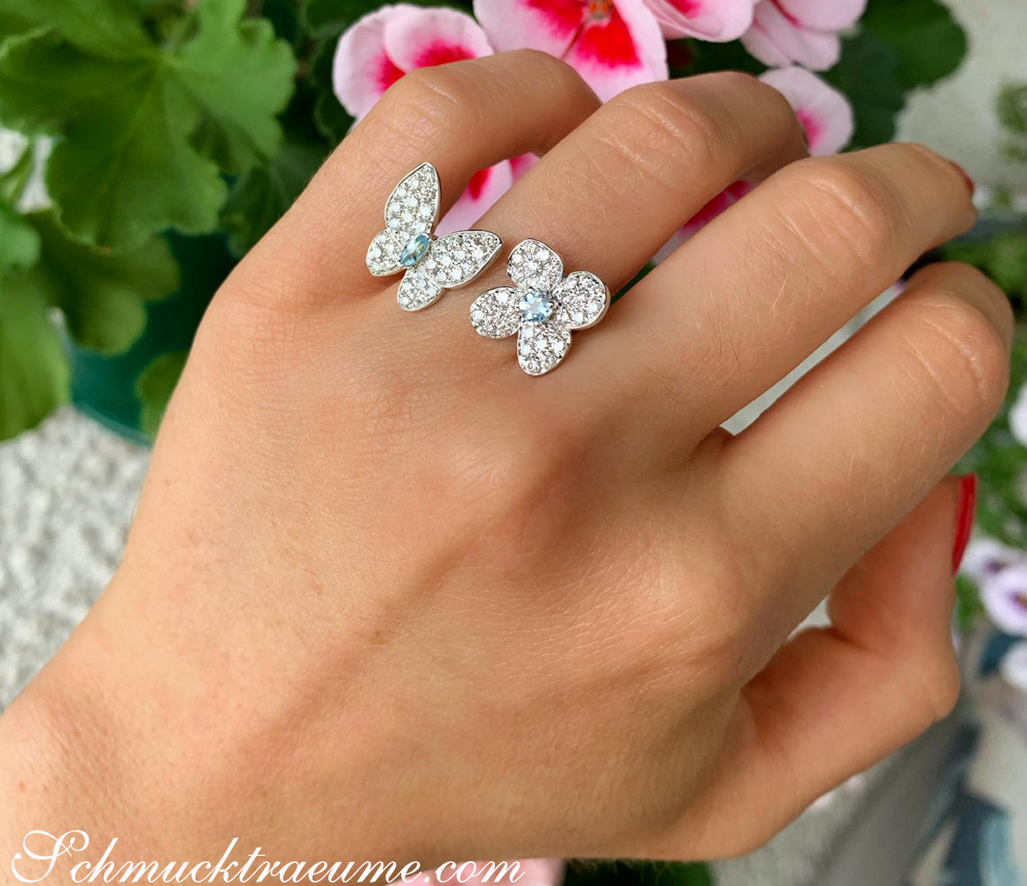 Femininer Brillanten-Ring "Schmetterling trifft Blüte" auf Hand, im Hintergrund Blüten und Blätter.