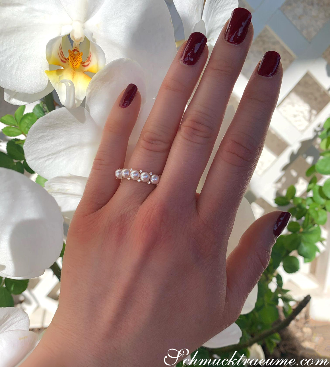 Akoya Perlenring mit Diamanten, Detailaufnahme, zarte Nahaufnahme, weibliche Hand, weißer Orchideenblüte im Hintergrund