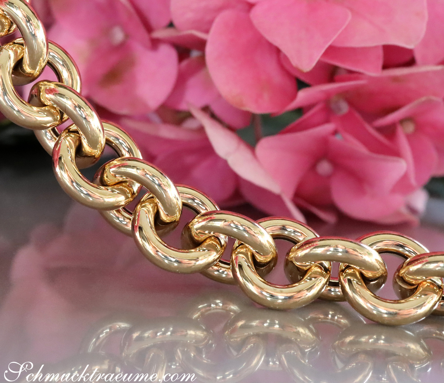 Goldene Kette mit glänzenden Gliedern vor rosa Blüten