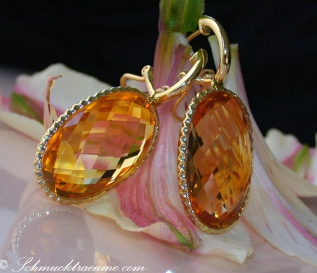 Gelbgold-Ohrringe mit Citrin-Steinen auf Blütenhintergrund Gelbgold-Ohrringe mit Citrin-Steinen auf Blütenhintergrund