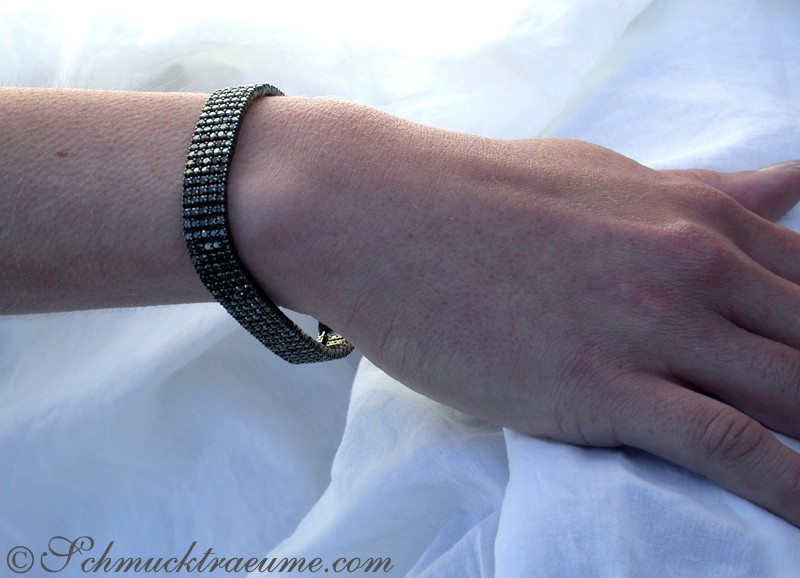 Schwarzes Armband mit Diamanten auf Hand vor weißem Hintergrund