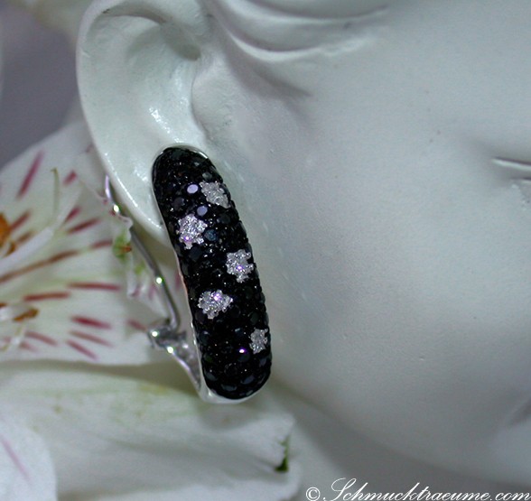 Schwarze Diamant-Tupfen-Ohrringe auf weißem Mannequin, Detailansicht mit Blume im Hintergrund.