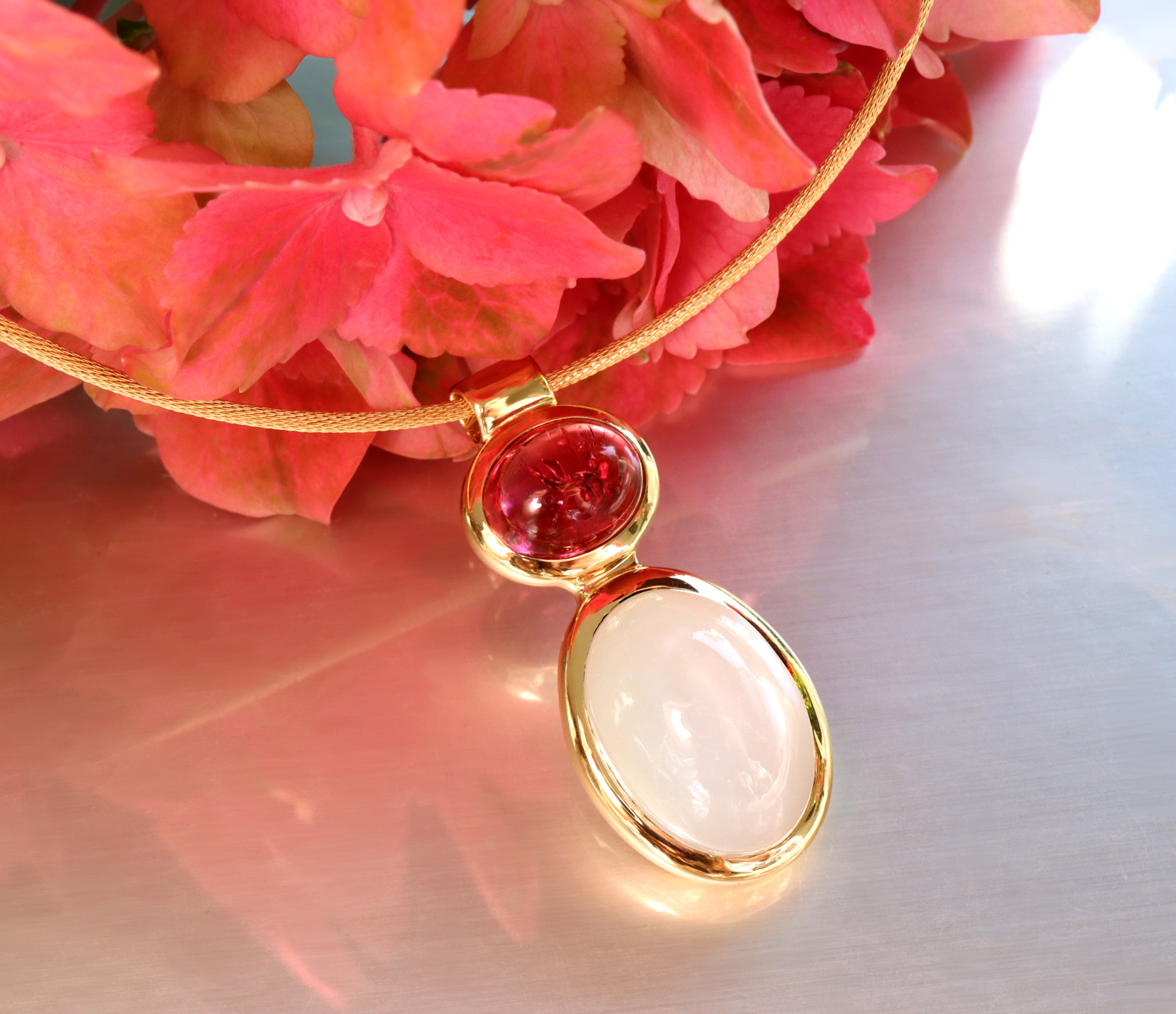 Goldene Halskette mit Rubellit und Mondstein, Blumen im Hintergrund.