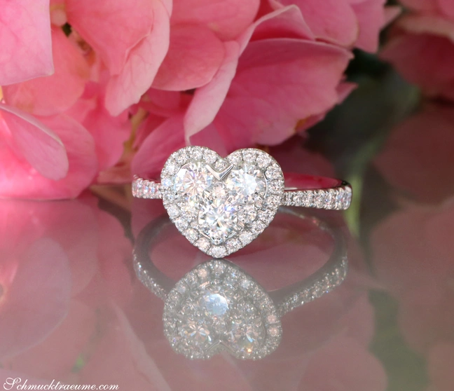 Herzring aus Weißgold mit VS-Brillanten, Detailaufnahme vor rosa Blüten. Herzring aus Weißgold mit VS-Brillanten, Detailaufnahme vor rosa Blüten.